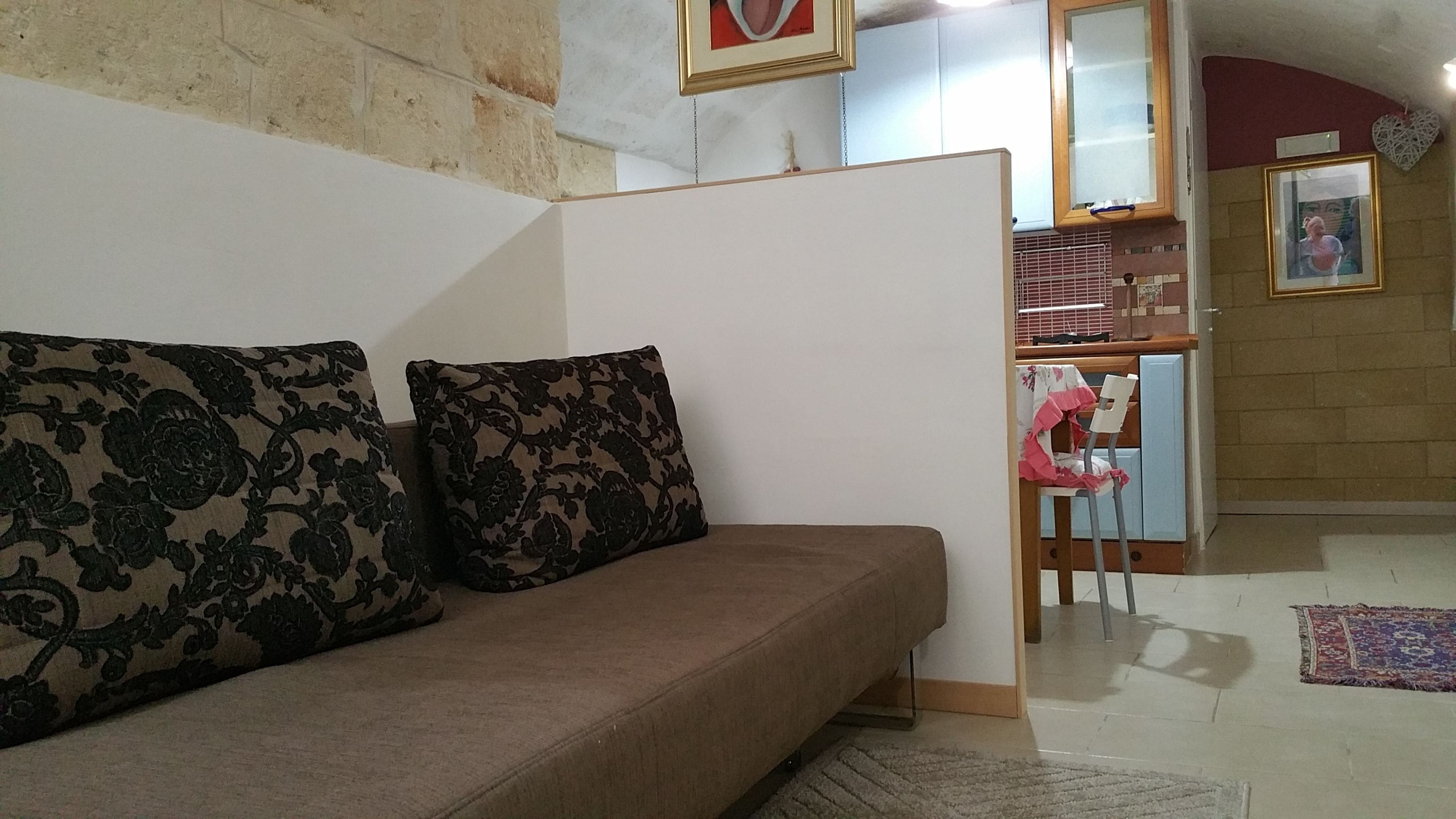 A living room with a sofa, a chair, and a kitchen area visible through an open door.