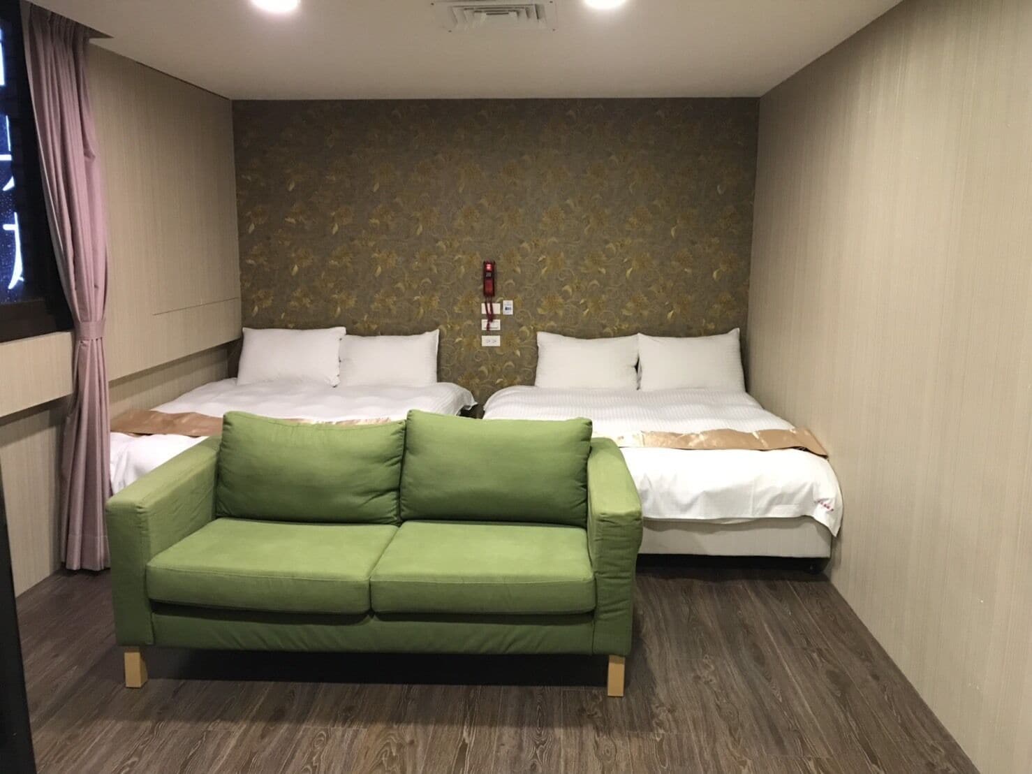 Une chambre d’hôtel avec deux lits, un canapé vert et un mur à motifs.
