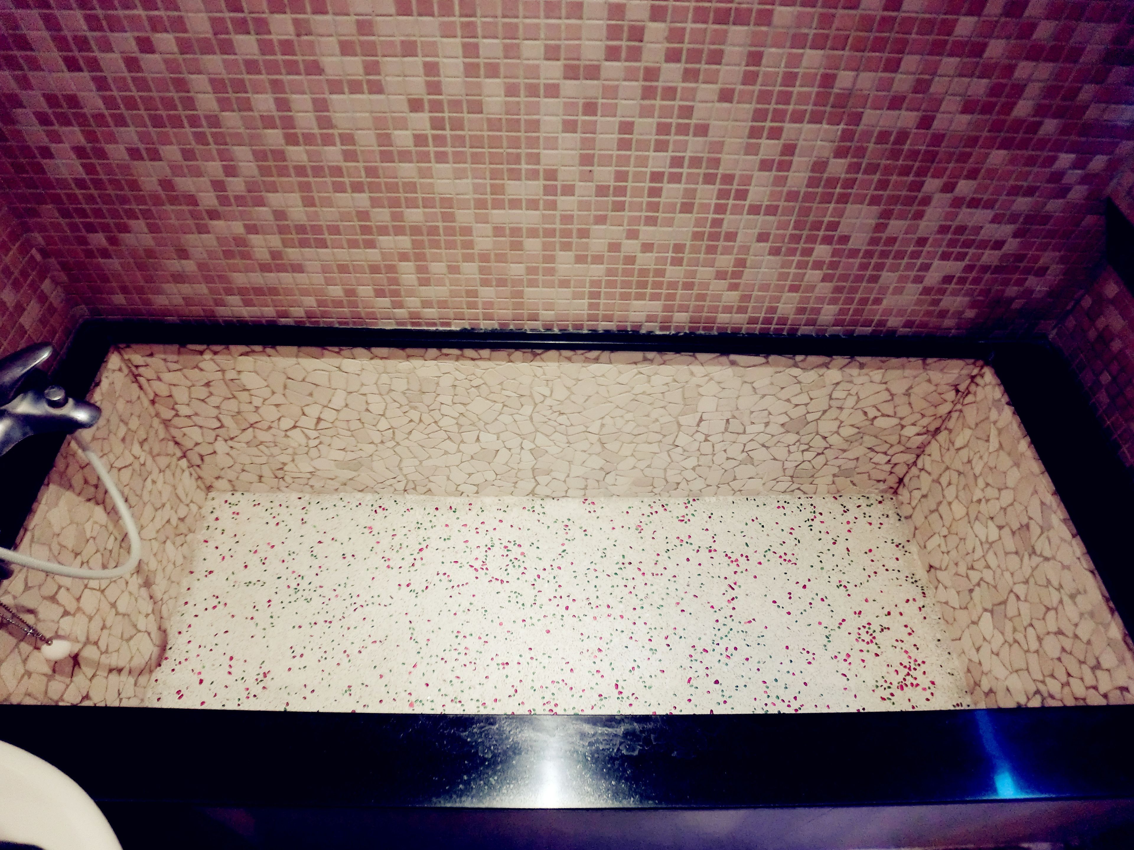 Eine Badewanne mit Mosaikfliesen an den Wänden und einem weiß gefliesten Boden.