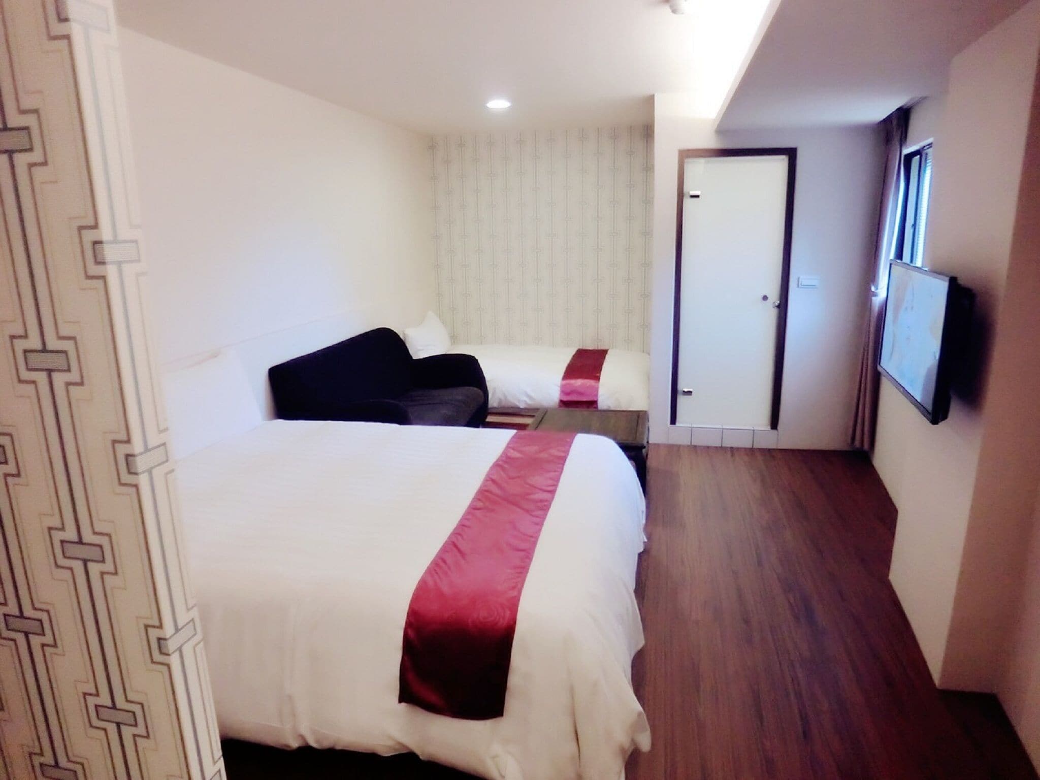 A hotel room with a large bed, a smaller bed, a TV, and a door leading to another room.