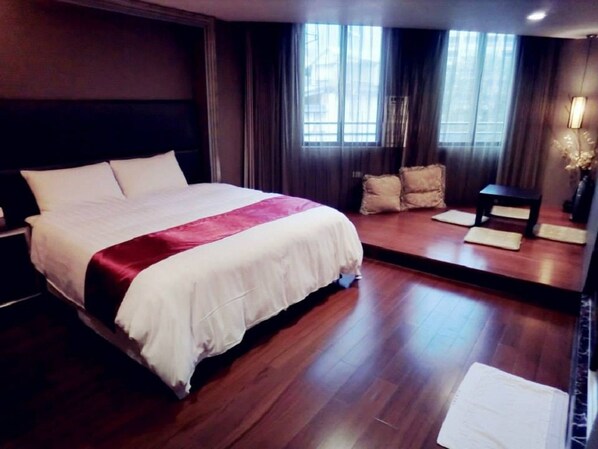 A hotel room with a large bed, wooden flooring, a small table, and a mirror.