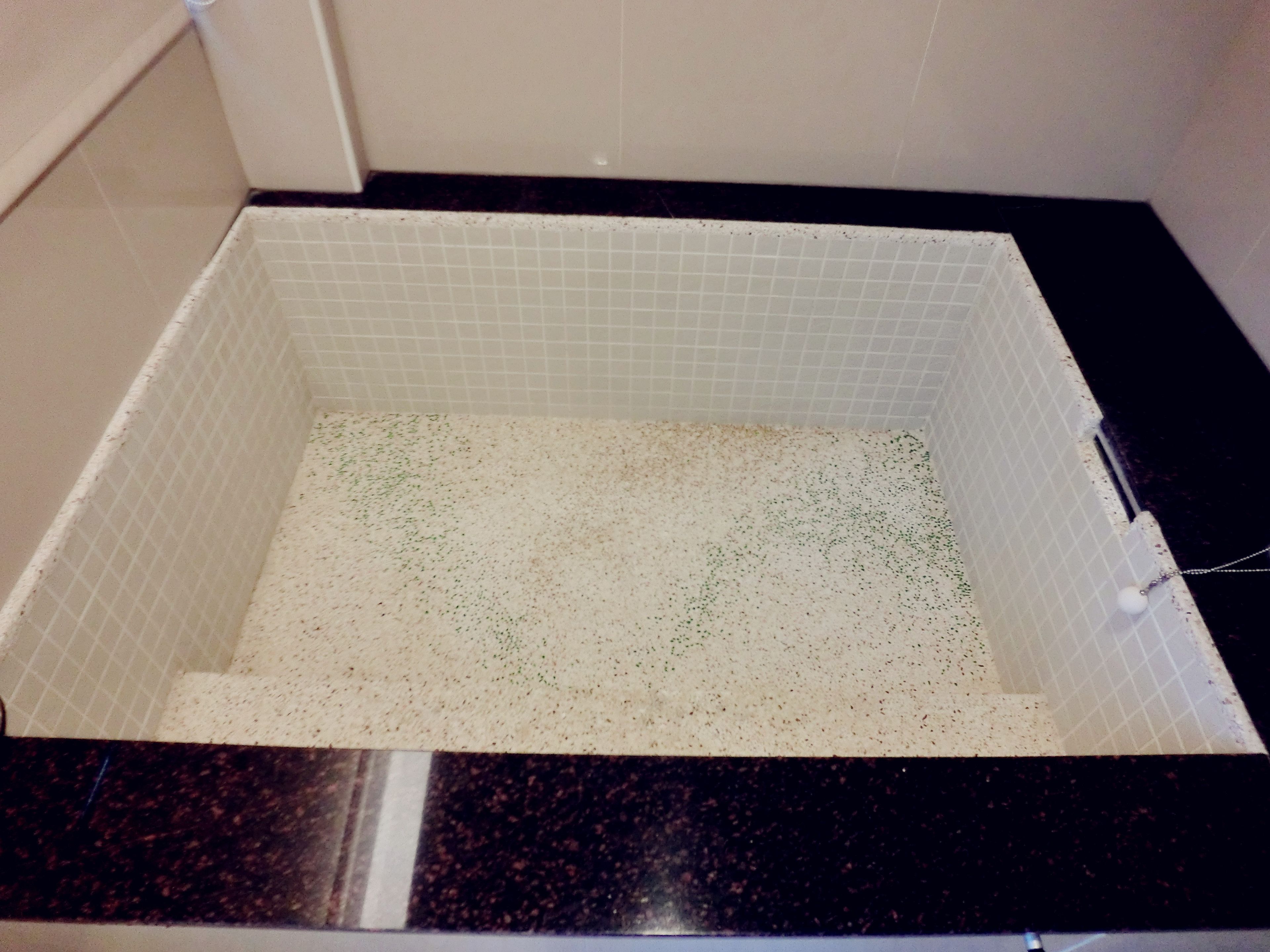 Un baño con piso de baldosas blancas y encimera negra.
