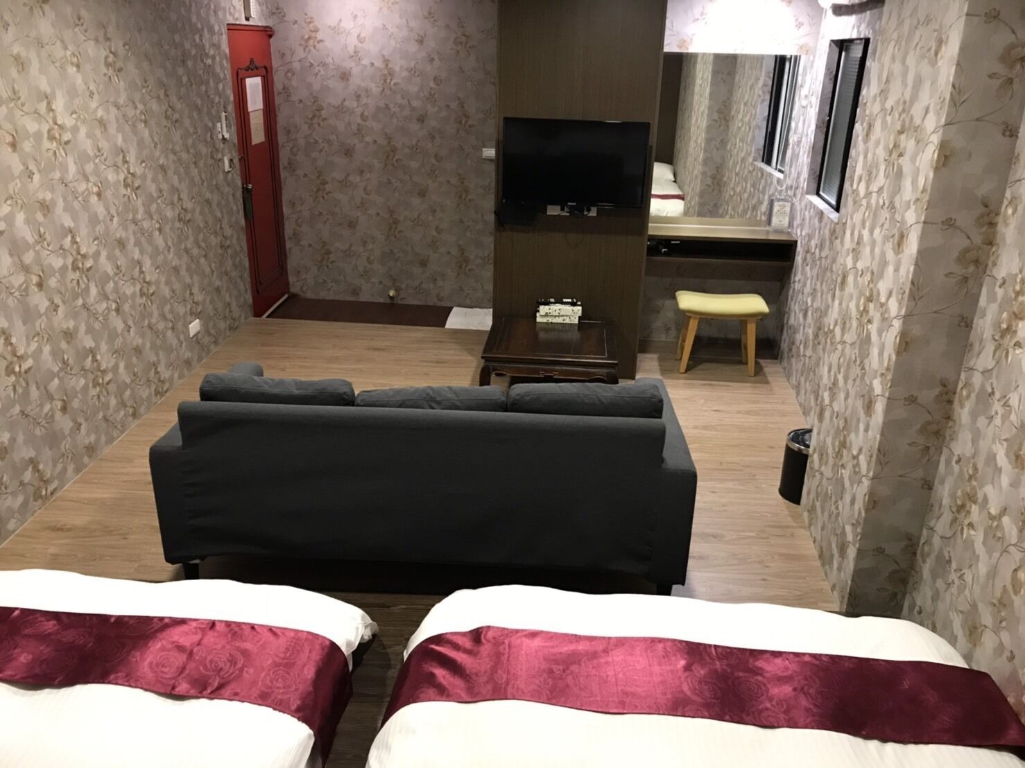 Una habitación de hotel con sofá cama, escritorio con televisor, taburete pequeño y armario.