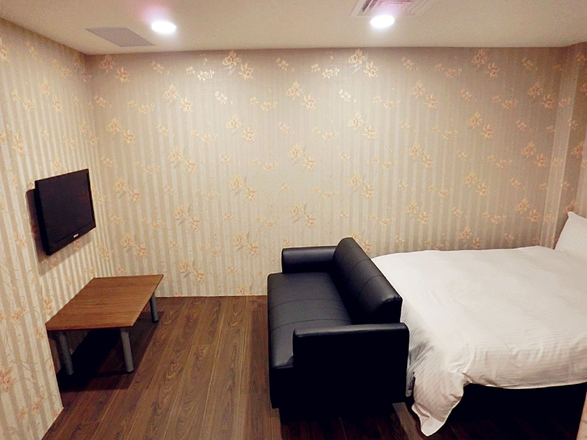 A hotel room with a bed, a sofa, a small table, and a TV mounted on the wall.