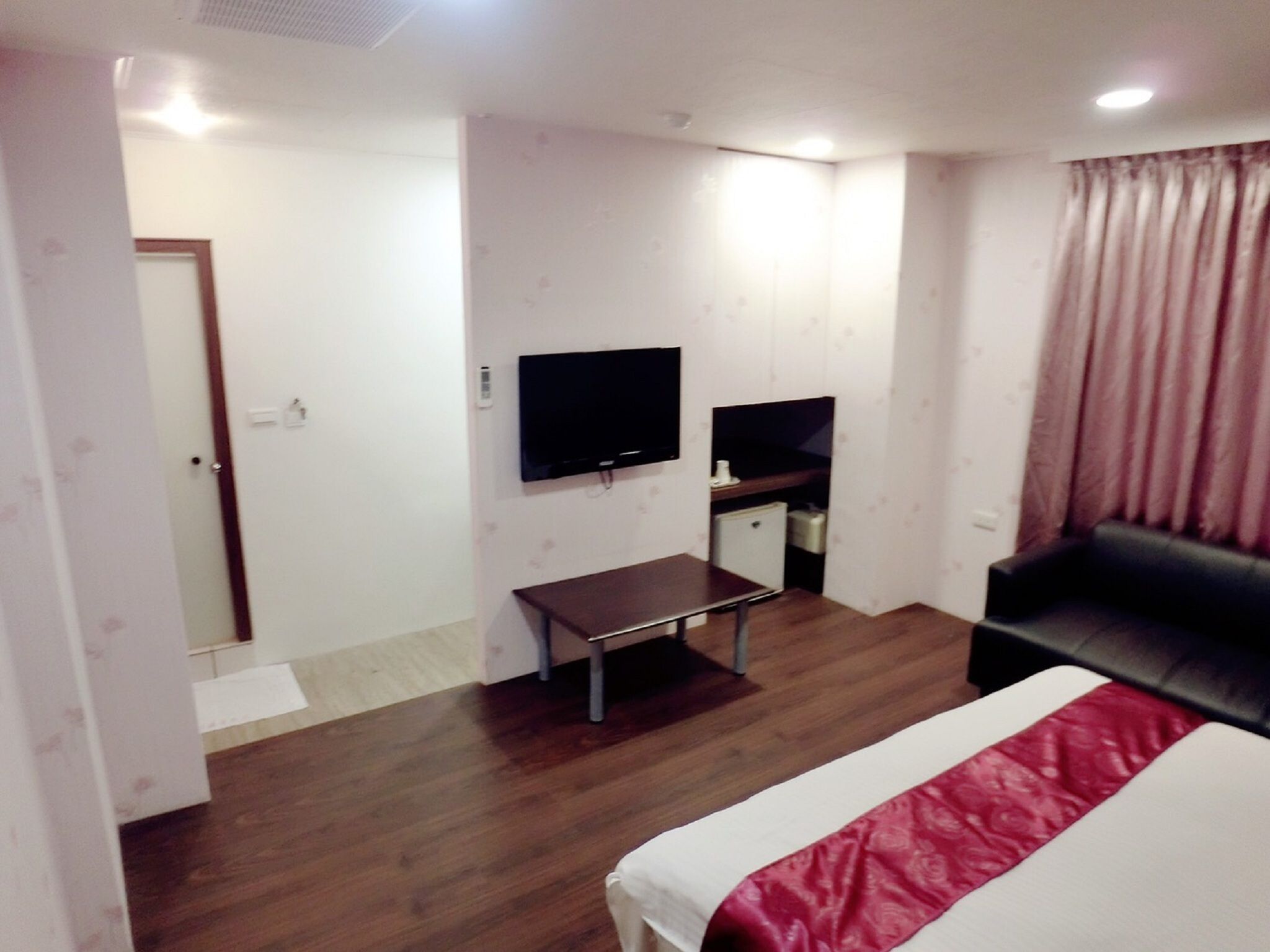 A hotel room with a bed, a TV, a desk, and a small kitchenette.