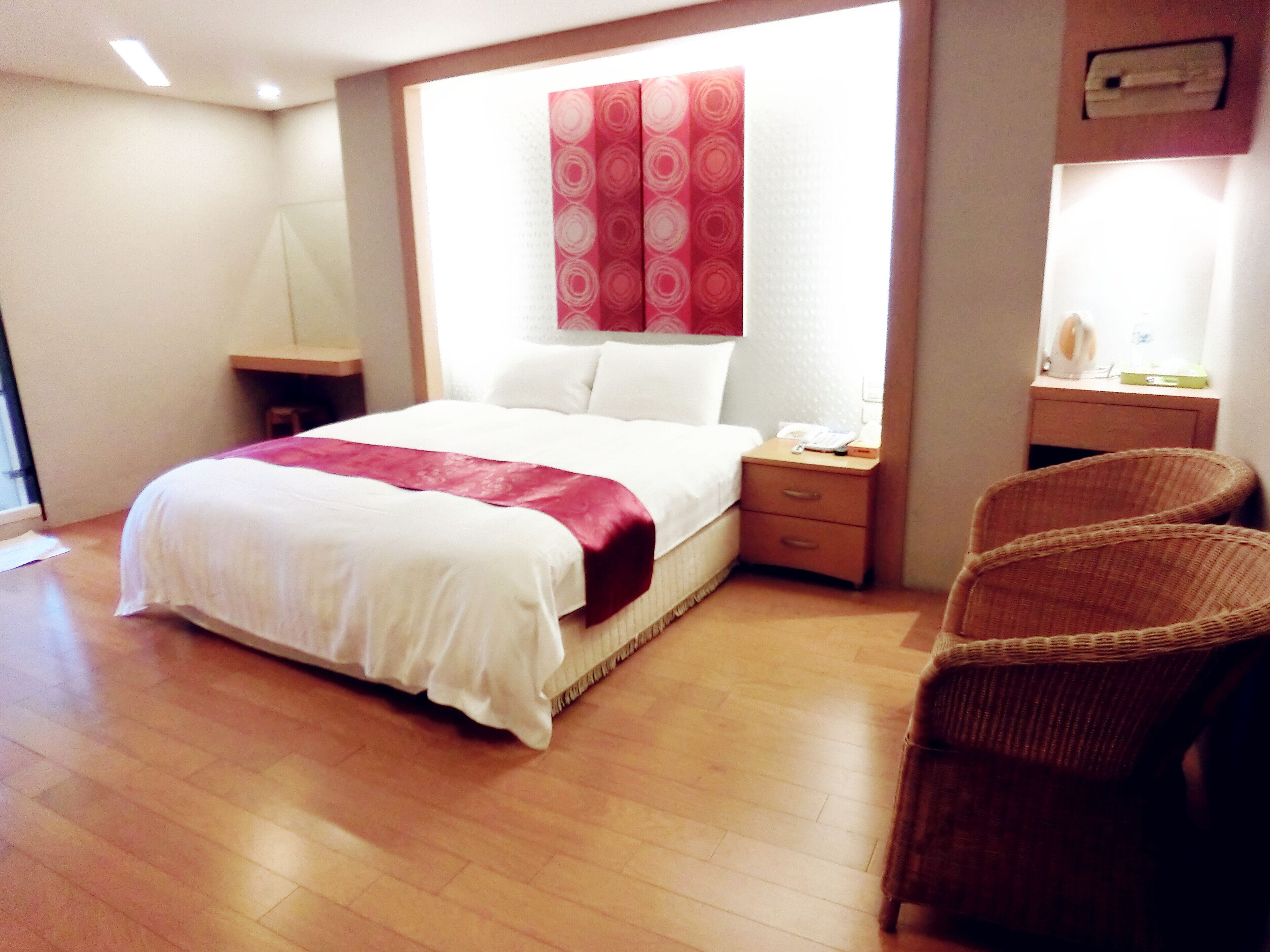 A hotel room with a large bed, a nightstand, a chair, and a desk with a lamp.