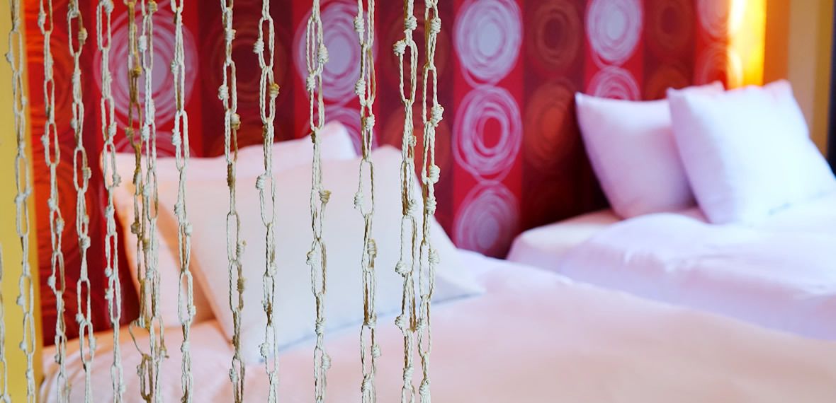 A bed with white bedding and a red patterned headboard.