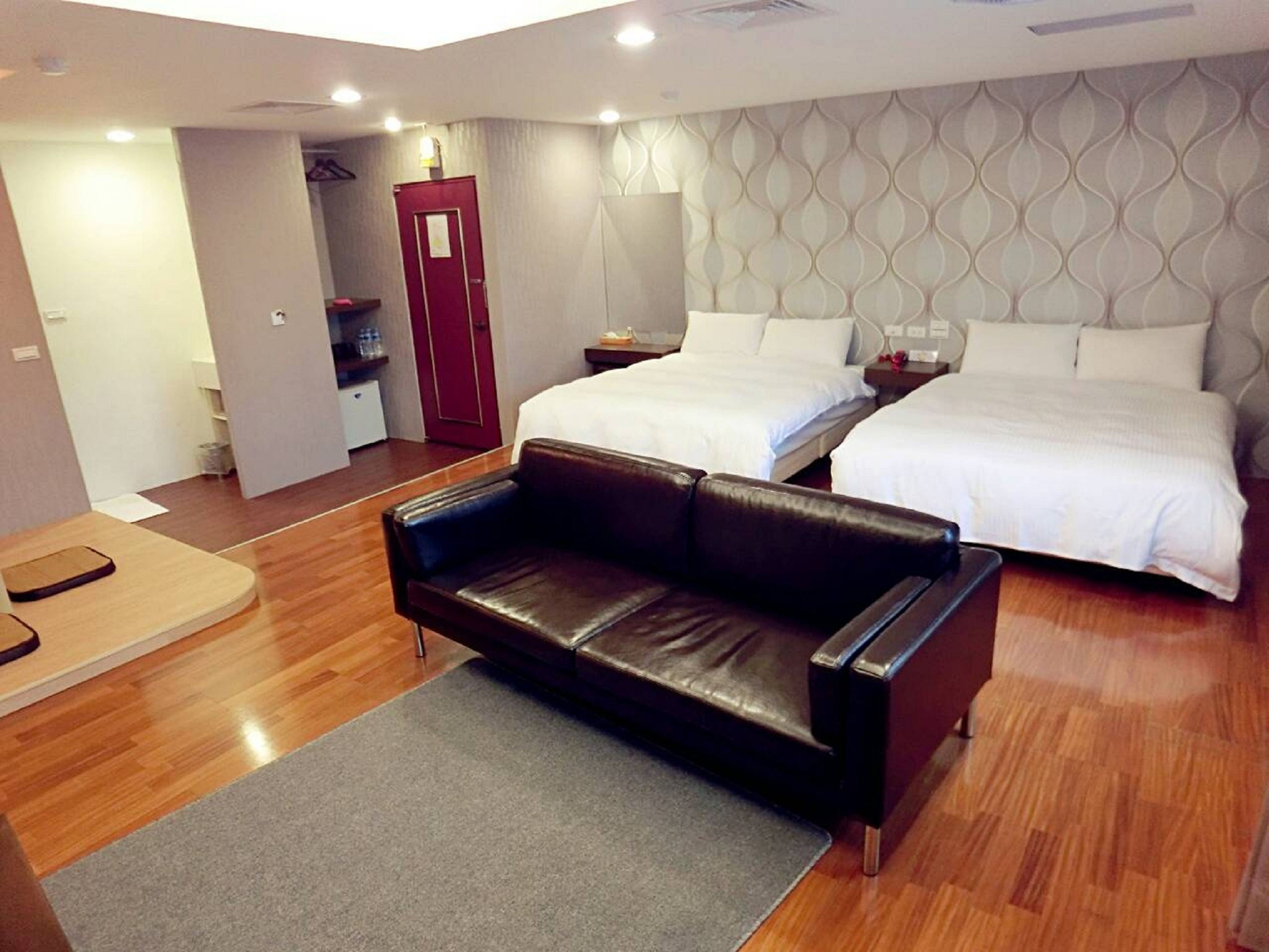 A modern hotel room with two beds, a leather sofa, and a small desk.