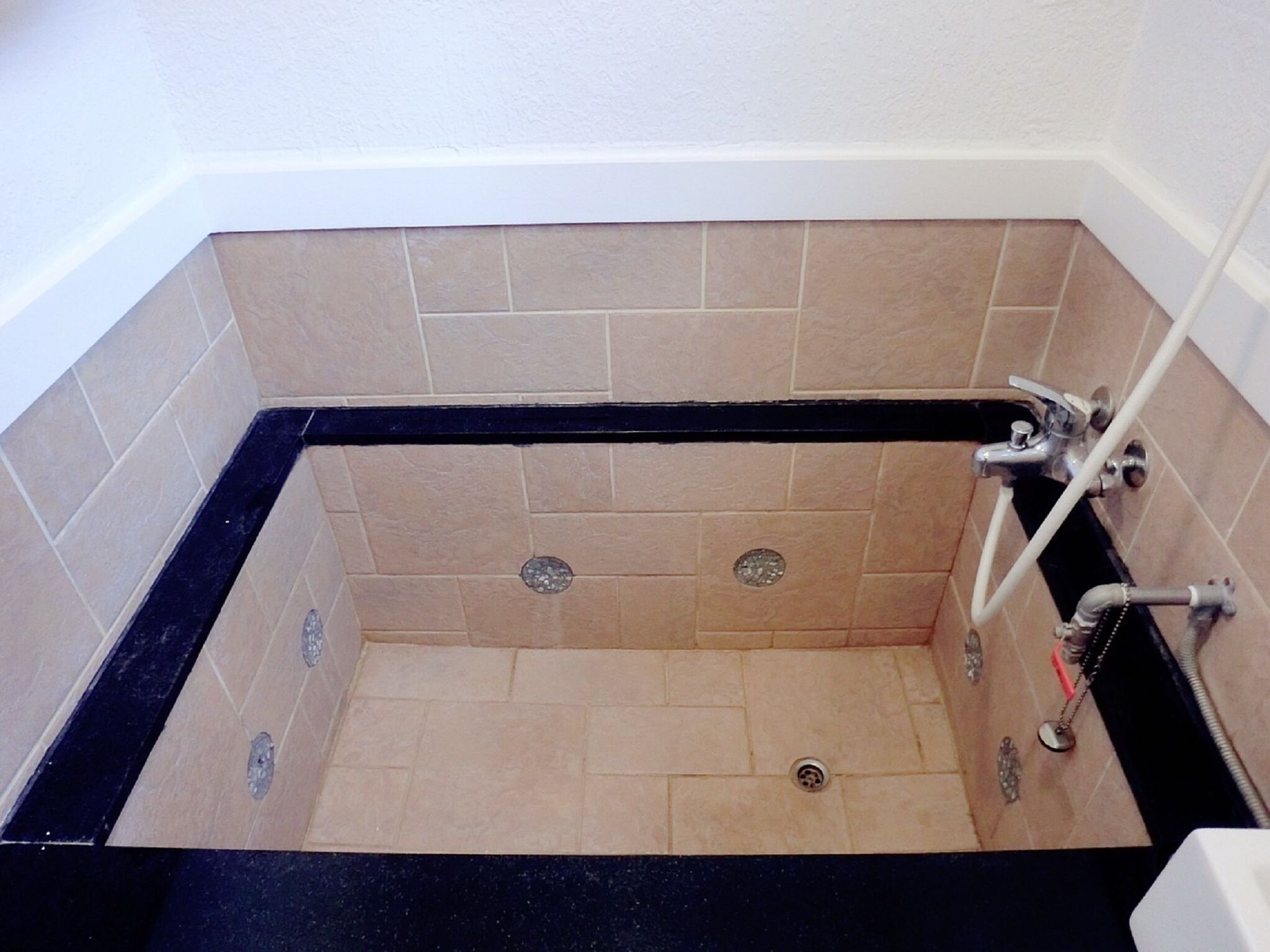 A corner bathtub with beige tiles, a black edge, and a showerhead.