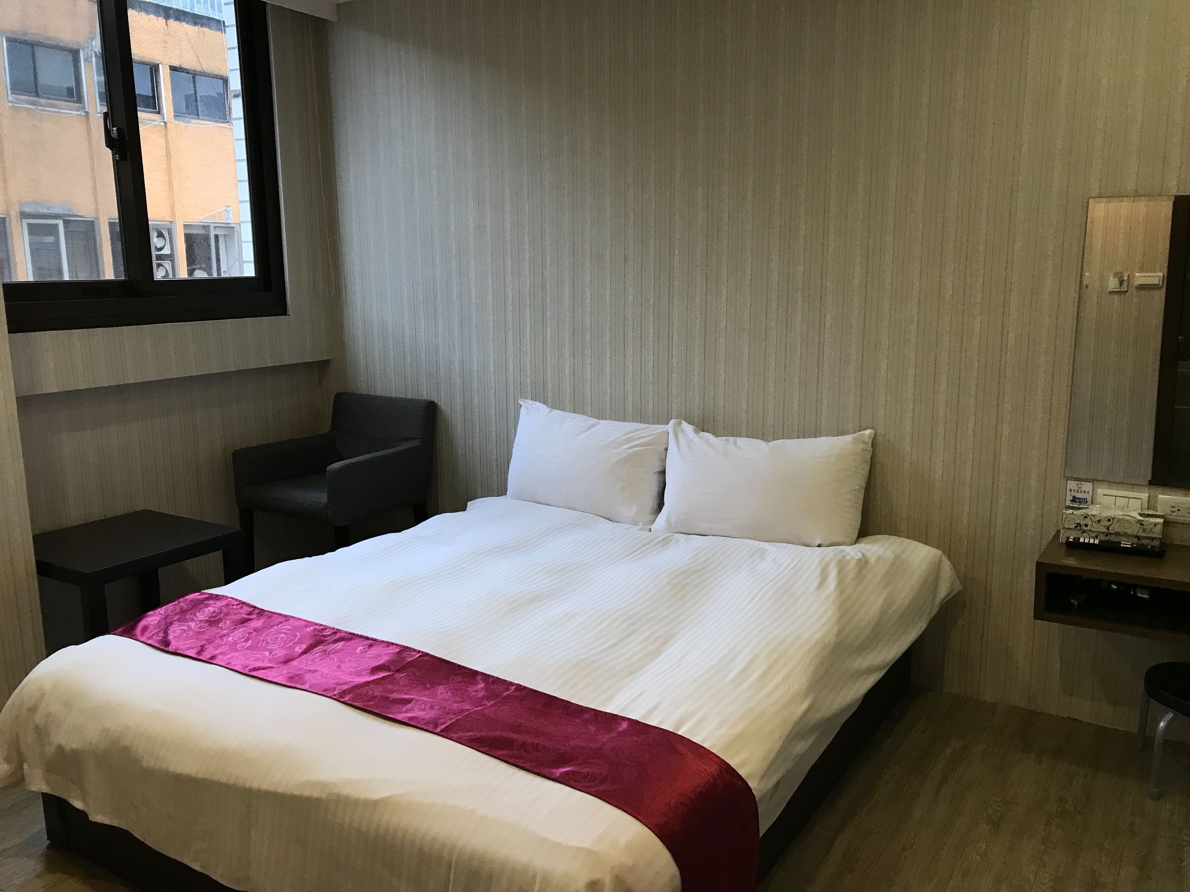 A hotel room with a bed, a chair, a desk, and a window.