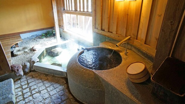 Un onsen japonais traditionnel, avec une source d’eau chaude alimentée par des pierres, des murs en bois et un sol carrelé.