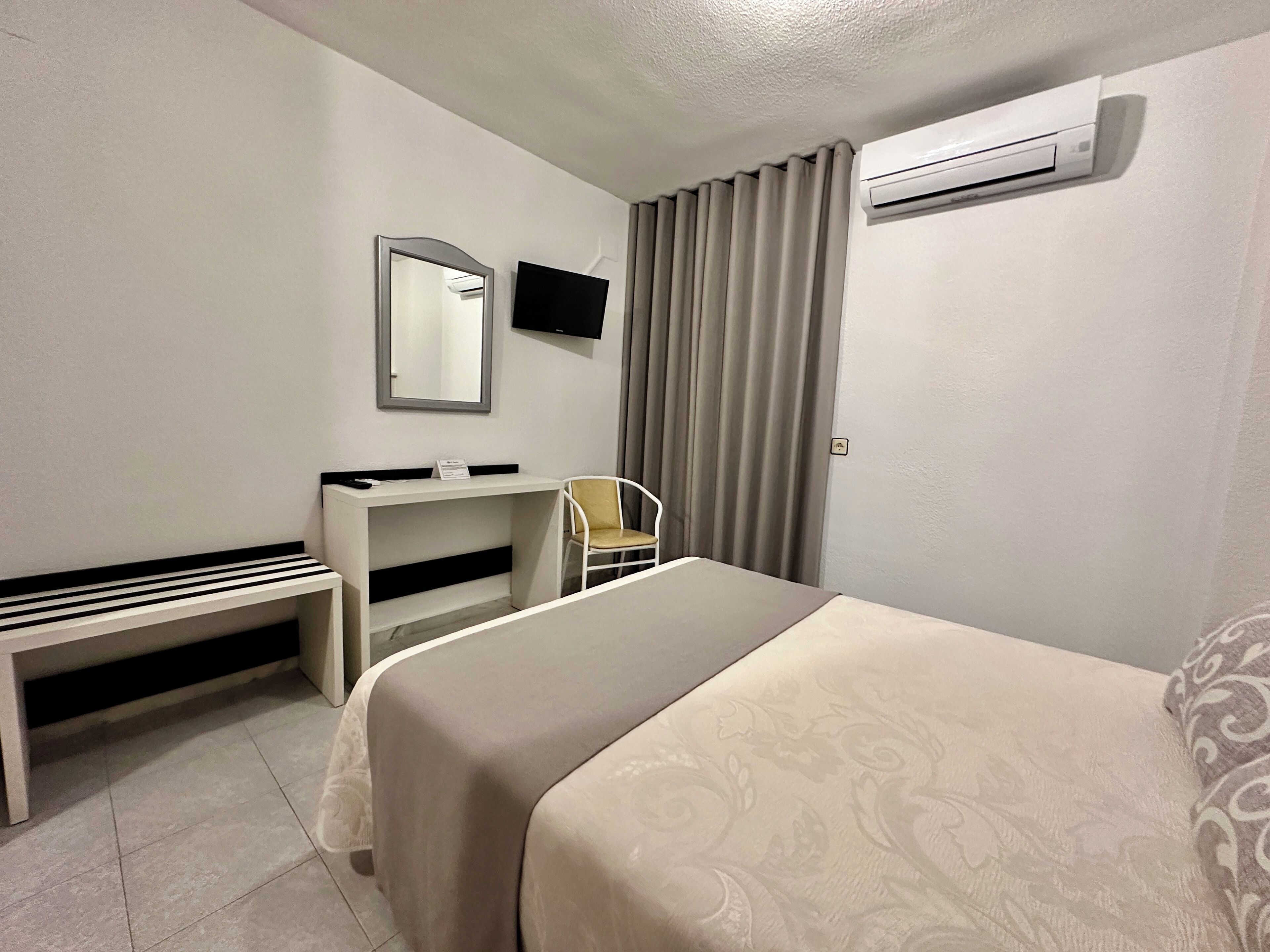 Una habitación de hotel con cama, escritorio, silla, televisor y aire acondicionado.
