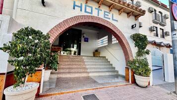 Una entrada de hotel con un arco destacado, una escalera que lleva a la entrada y plantas en macetas en la base.