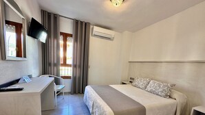 A hotel room with a bed, a desk, a chair, a TV, and an air conditioning unit. - Hotel El Paraiso (Aguilas)