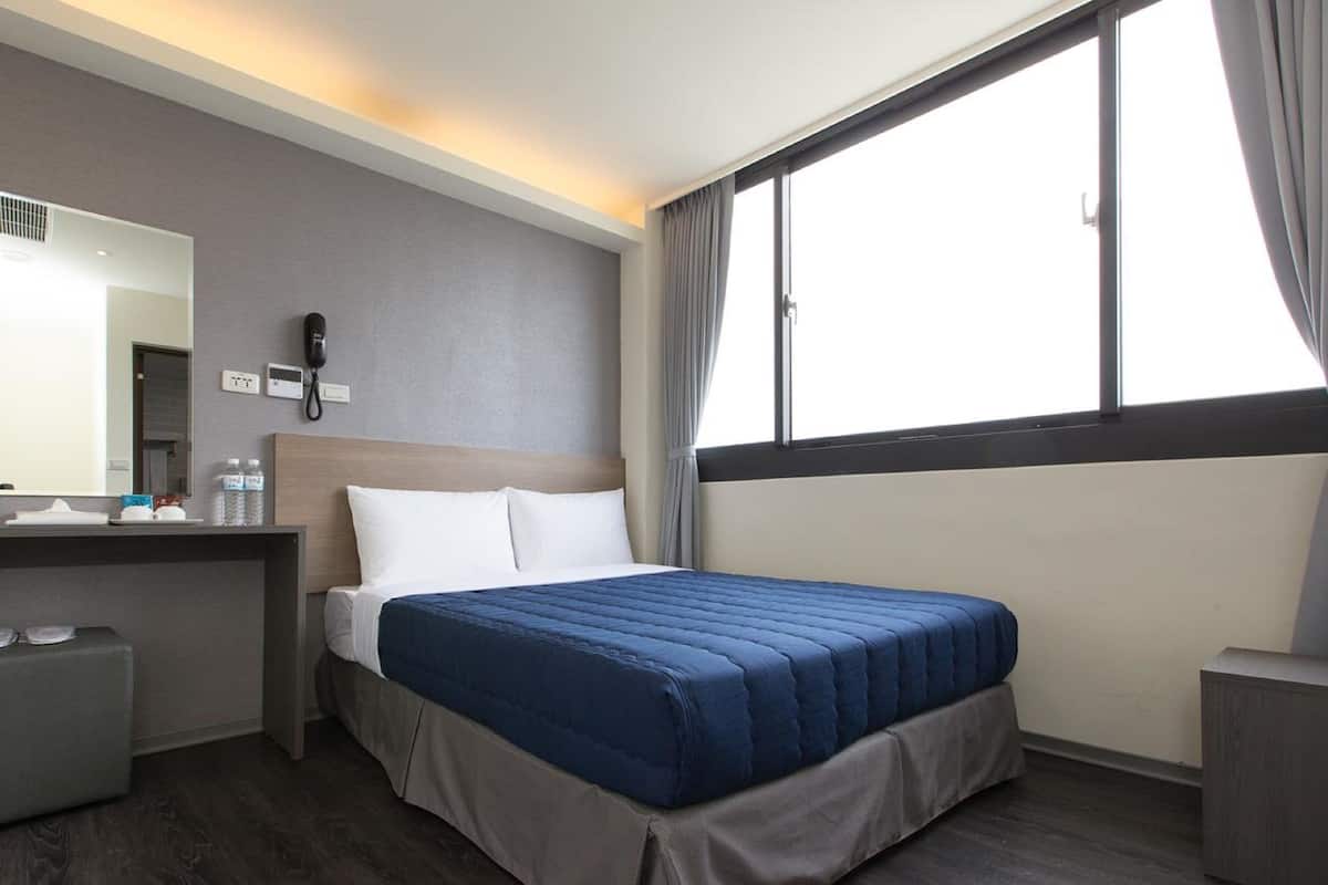 A hotel room with a bed, a desk with a phone, a mirror, and a window with curtains.