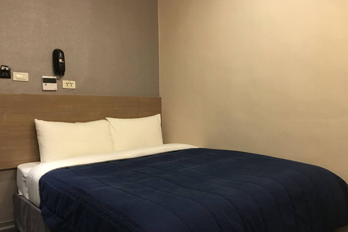 A hotel room with a bed, a wooden headboard, a telephone, and a wall socket.