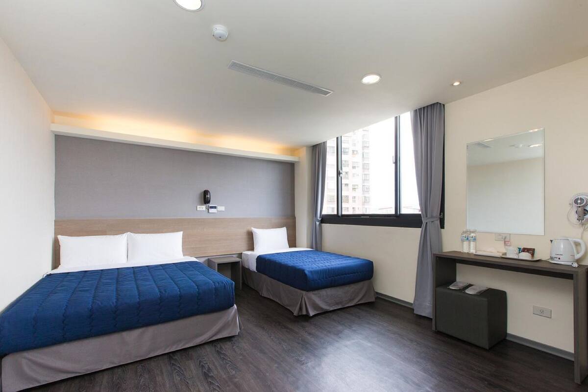 A hotel room with two beds, a desk, a mirror, and a window with curtains.