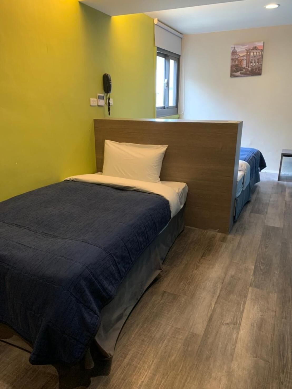 A single bed with a wooden headboard in a room with yellow walls and wooden flooring.