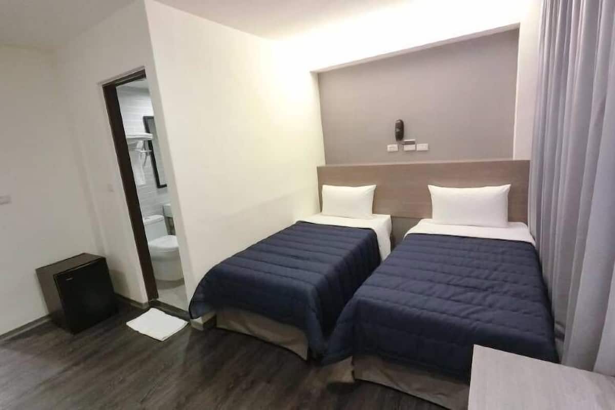 A hotel room with two beds, a small bedside table, a mirror, and a door leading to a bathroom.
