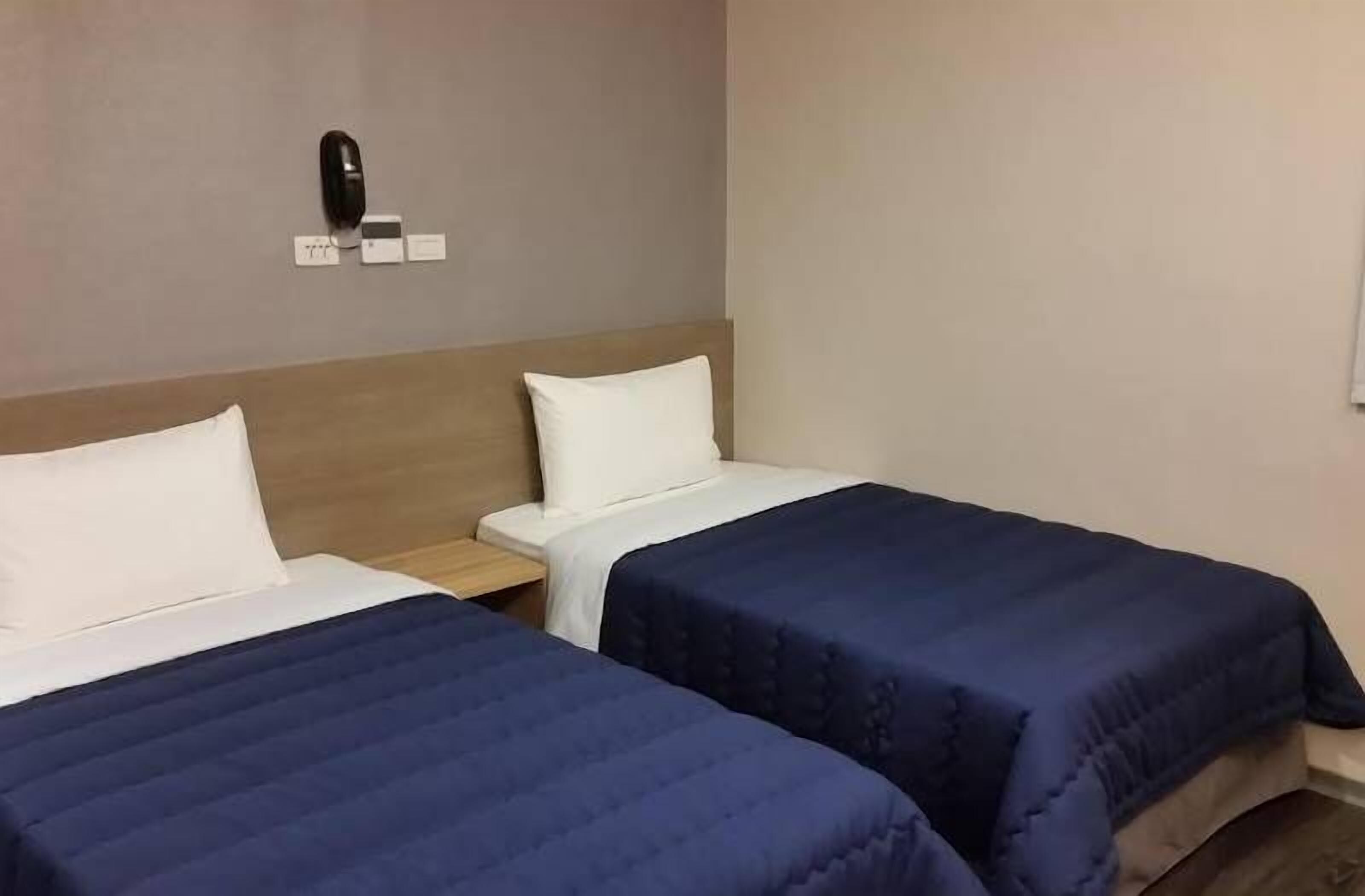 Habitación de hotel con dos camas, cada una con un almohadón blanco y una colcha azul. Hay una mesita de noche con un teléfono y una pequeña mesa entre las camas.
