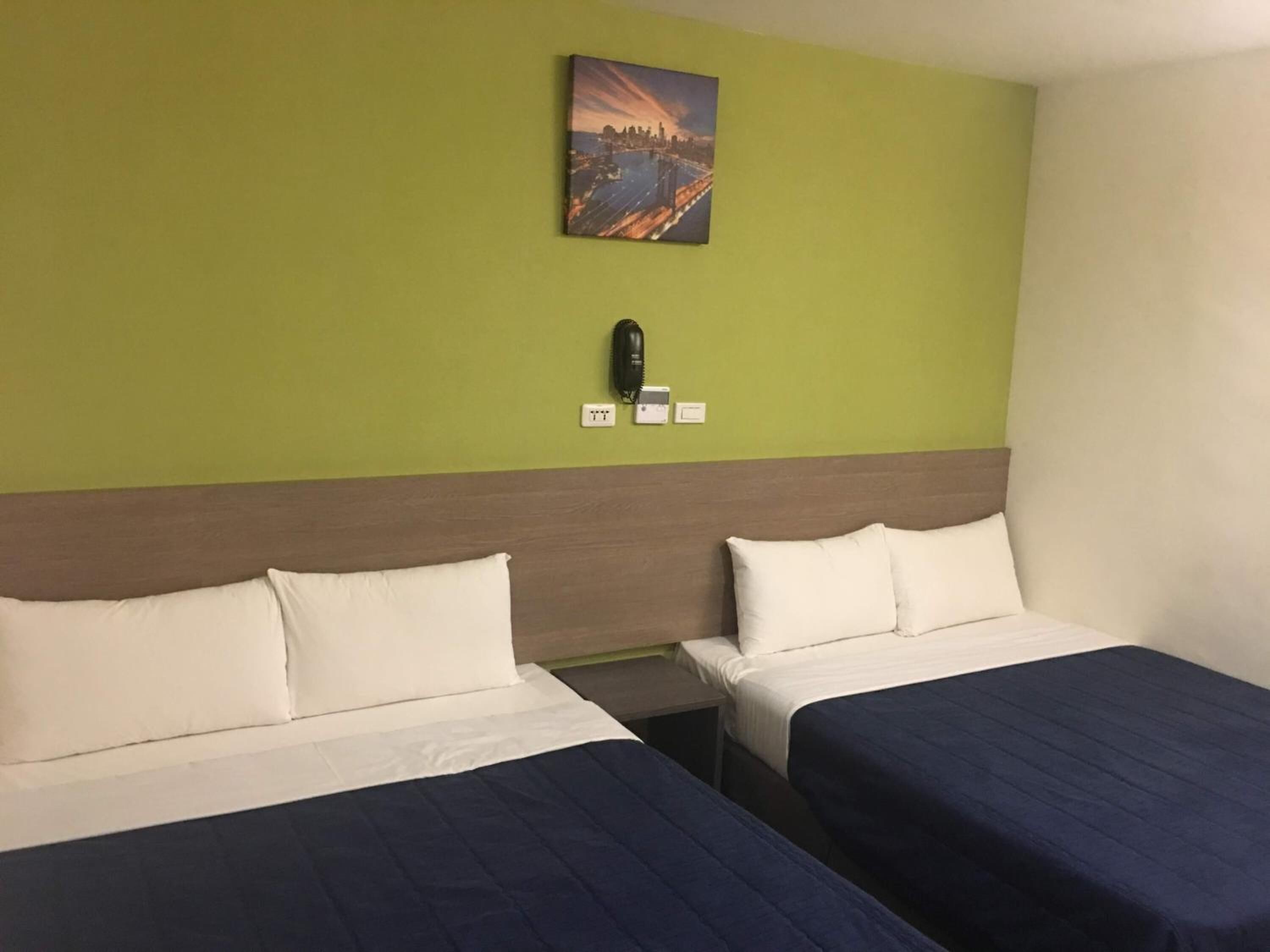 Una habitación de hotel con dos camas, una pared verde y un cuadro sobre las camas.