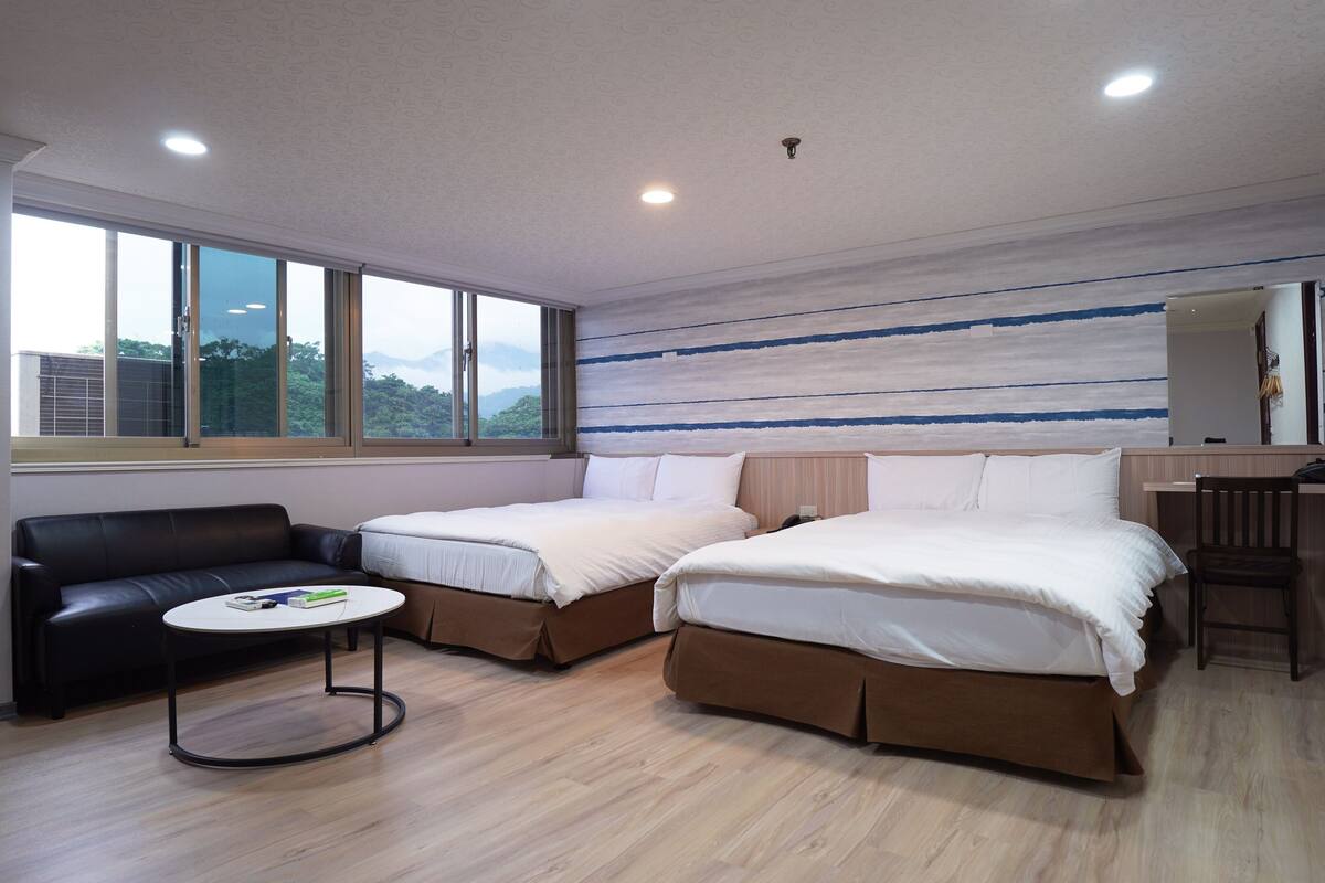 A hotel room with two beds, a sofa, a small table, and a desk.
