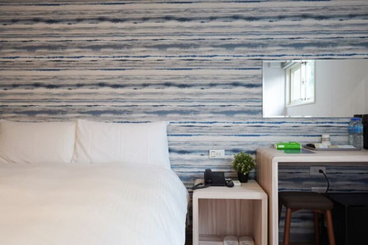 A hotel room with a bed, a desk with a phone, a small plant, and a mirror on the wall.