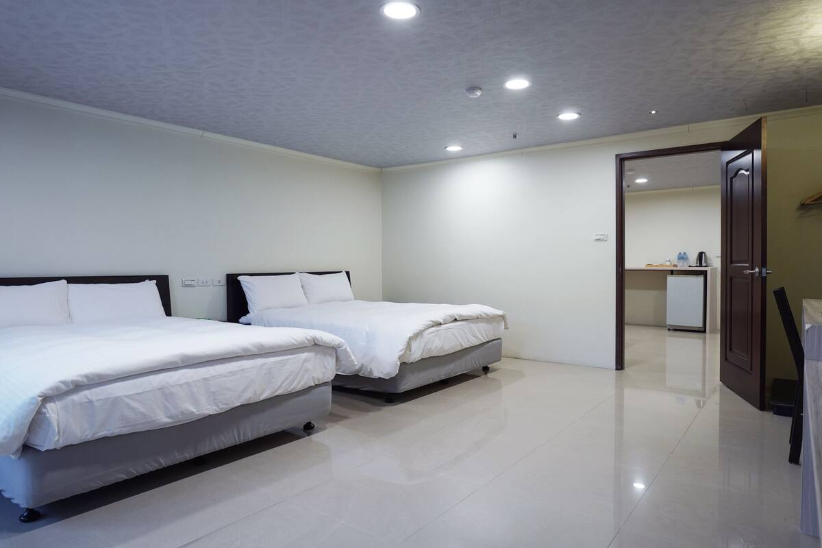 A hotel room with two beds, a small kitchenette, and a bathroom.