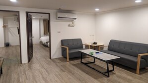 Una habitación moderna y bien iluminada con un sofá, dos sillones, una mesita y un equipo de aire acondicionado en la pared.