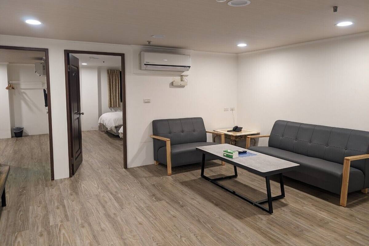 A modern, well-lit room with a sofa, two chairs, a small table, and an air conditioning unit on the wall.