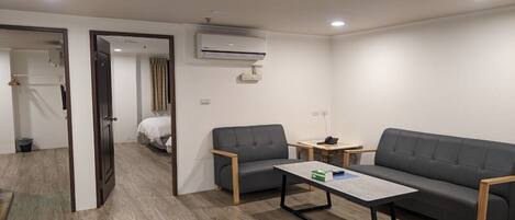 Una habitación moderna y bien iluminada con un sofá, dos sillones, una mesita y un equipo de aire acondicionado en la pared.