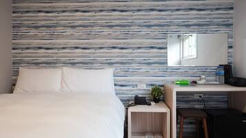 A hotel room with a bed, a desk with a computer, a phone, and a small plant.