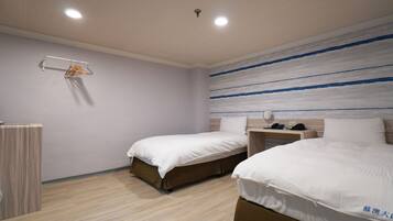 A hotel room with two beds, a bedside table with a lamp, a hanging clothes rack, and a wall with horizontal stripes.