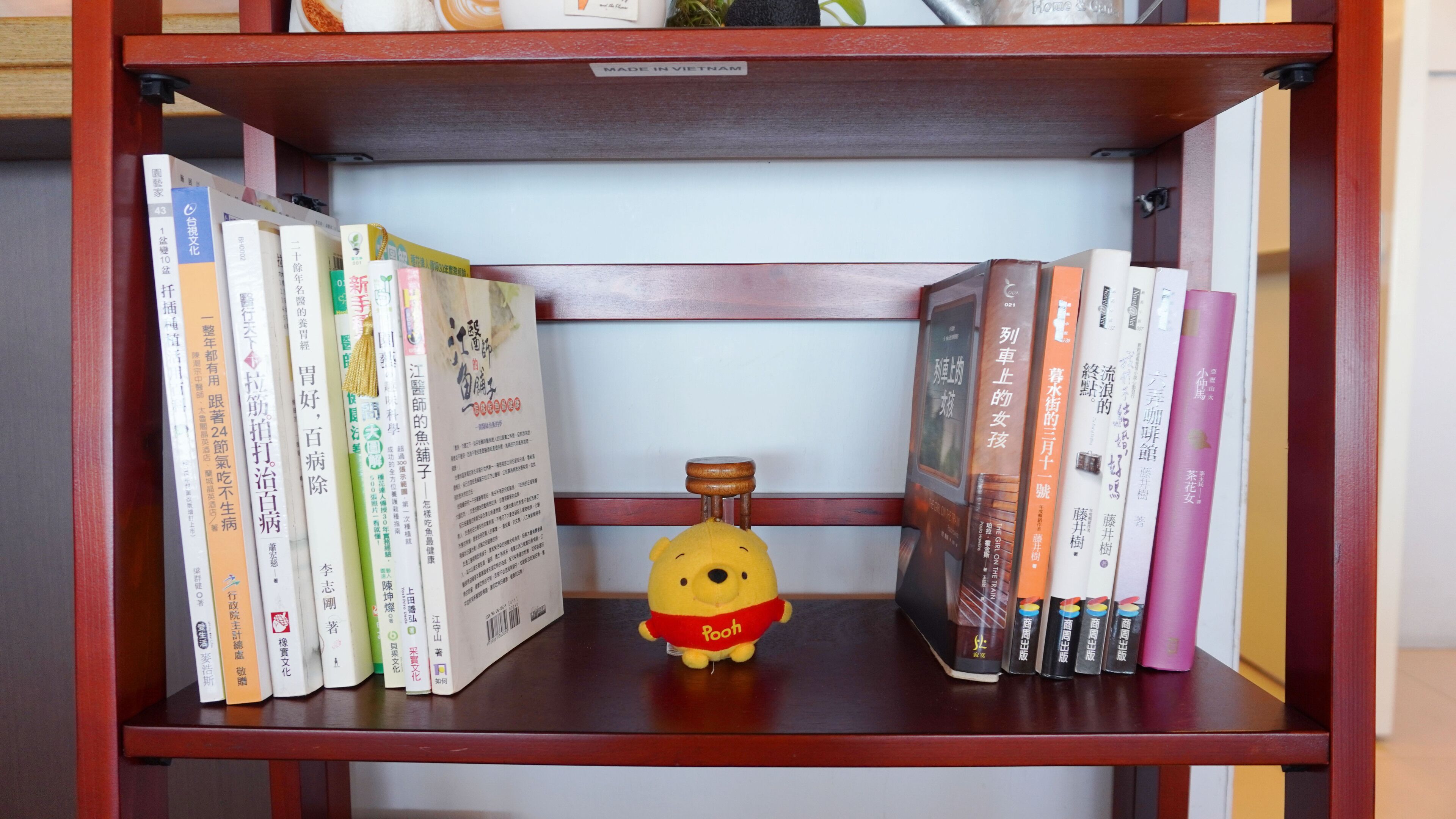 A bookshelf with a variety of books and a small yellow bear figurine.