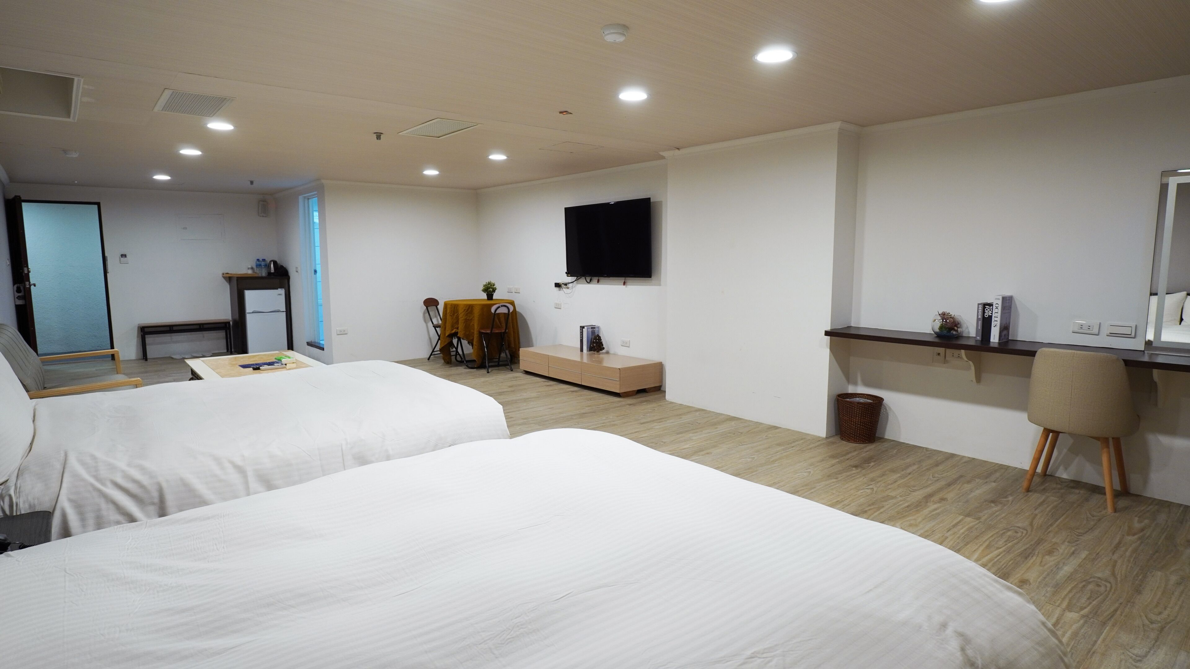 A hotel room with two beds, a desk, a chair, a TV, and a small table with a plant.