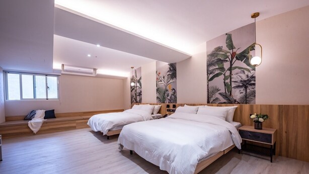 Un dormitorio moderno con dos camas, un banco, una mesita de noche y una lámpara fijada a la pared.