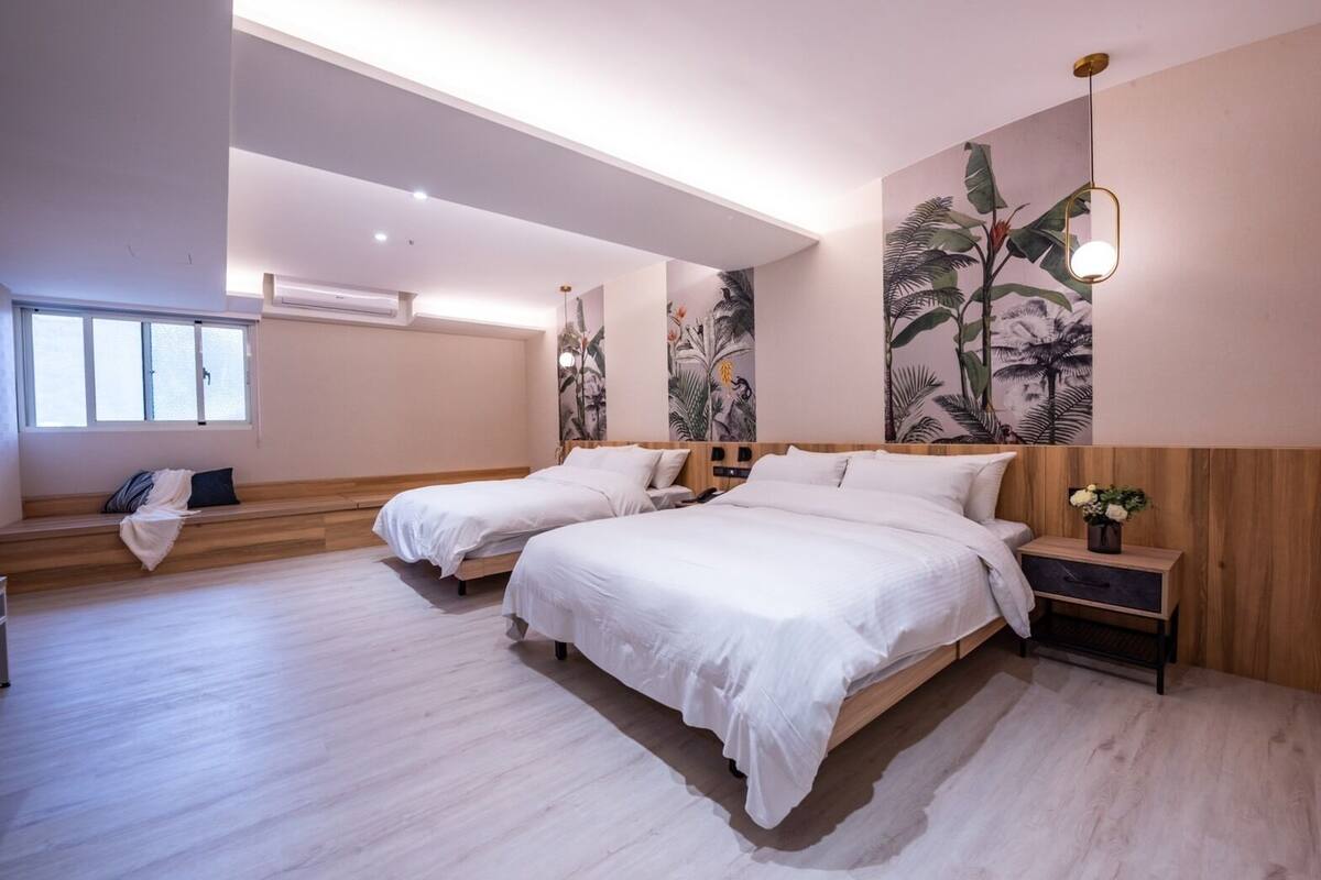 A modern bedroom with two beds, a bench, a nightstand, and a wall-mounted light fixture.