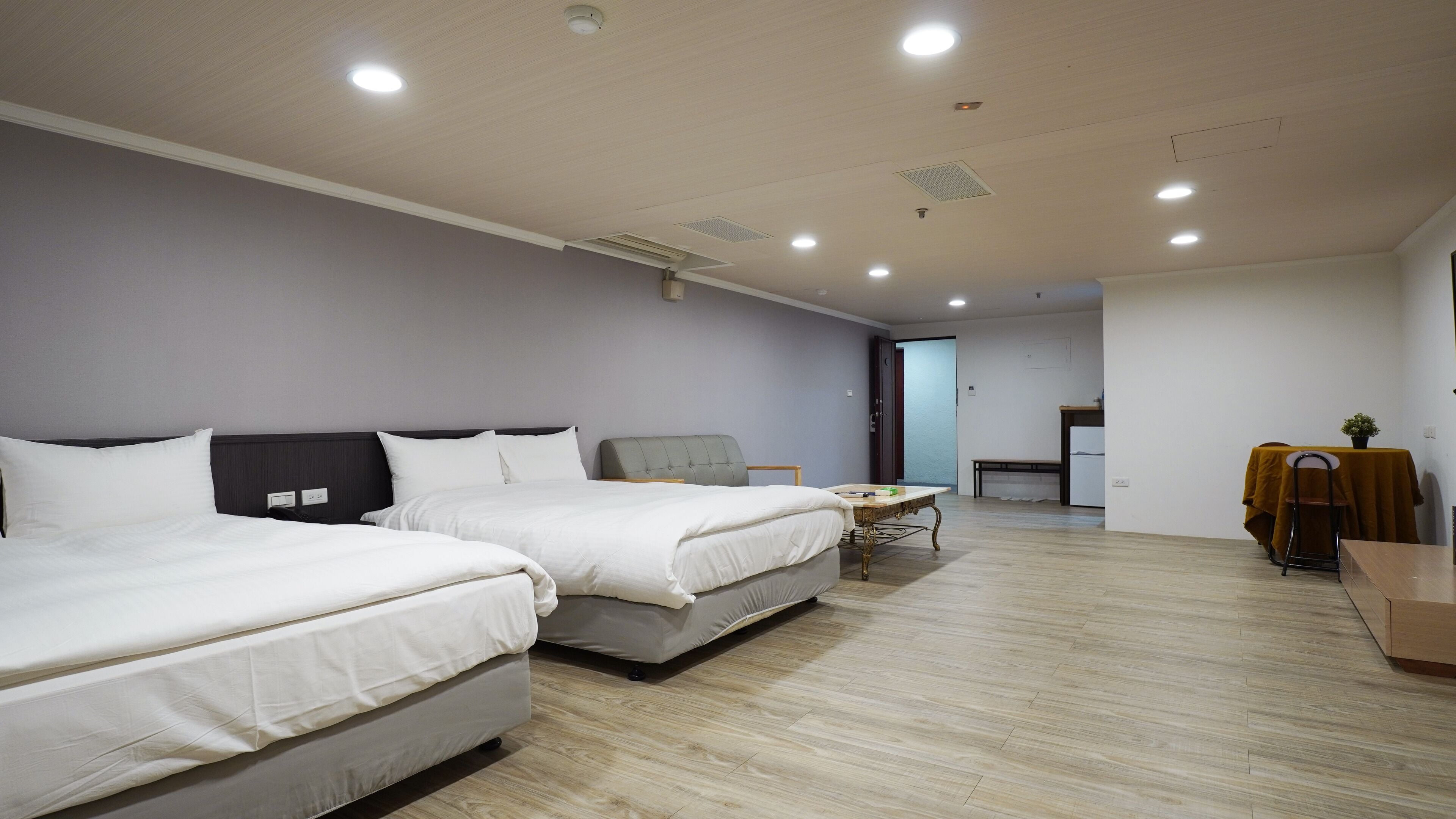 A hotel room with two beds, a small table, and a kitchenette area.