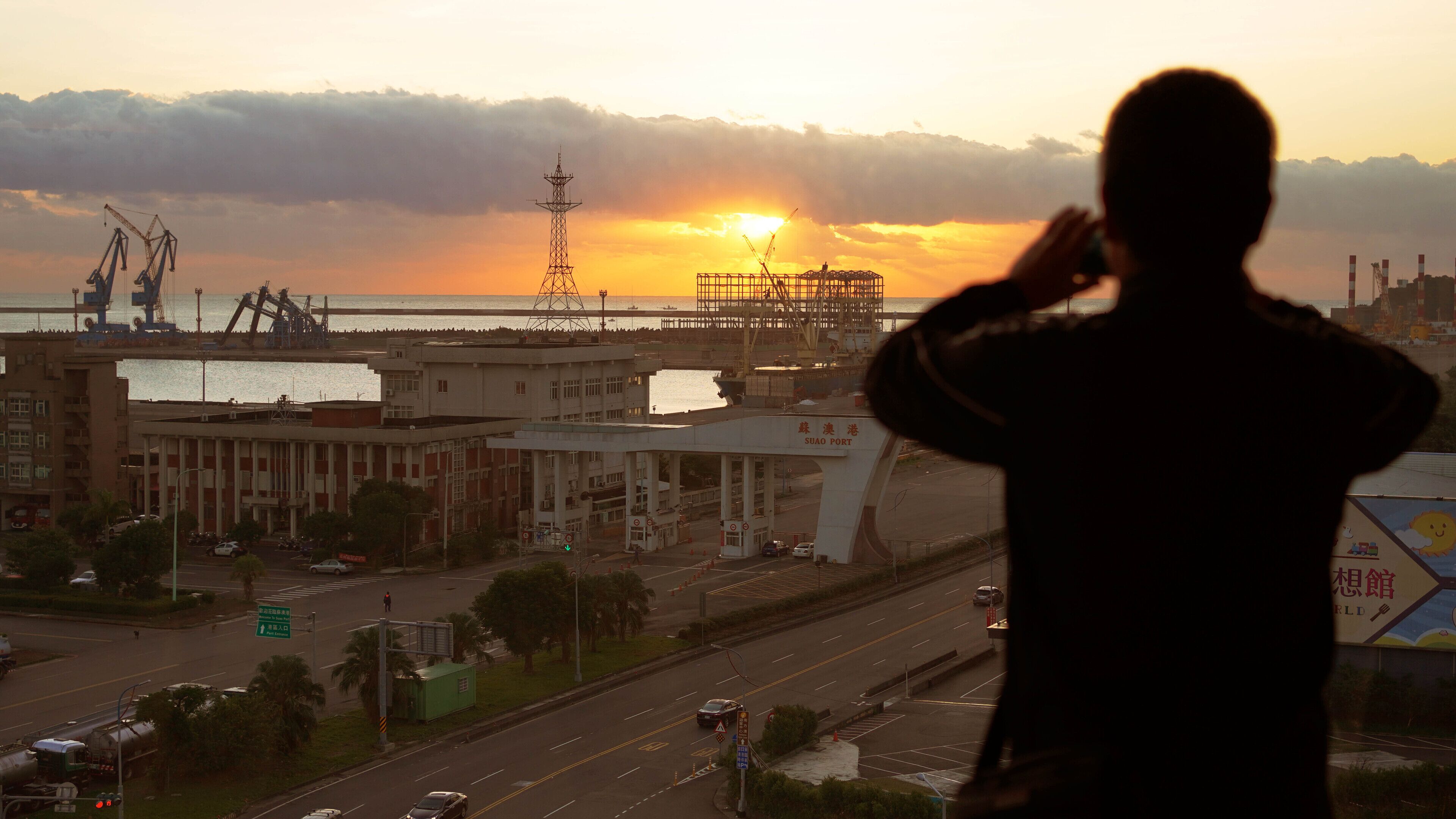 Eine Silhouette einer Person mit Blick auf einen Hafen und Industriegebäude.