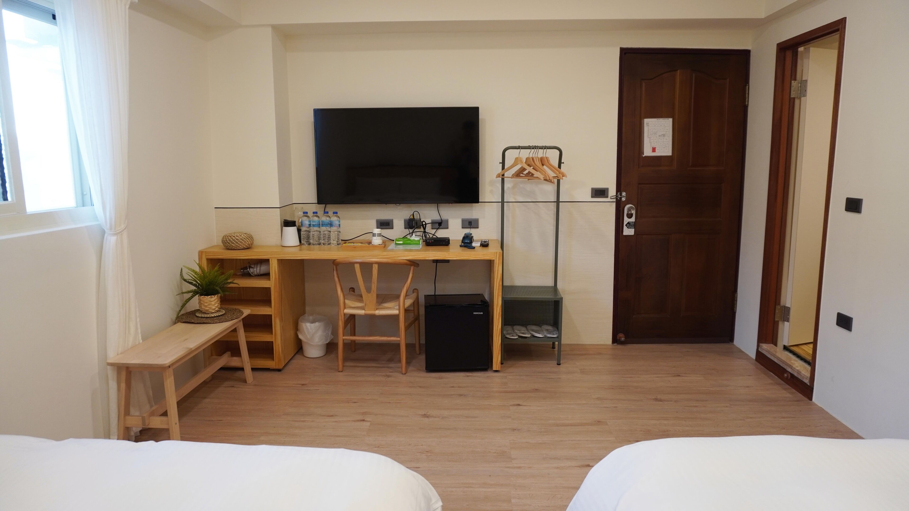 A small, tidy room with a wooden desk, a television, a bed, and a door.