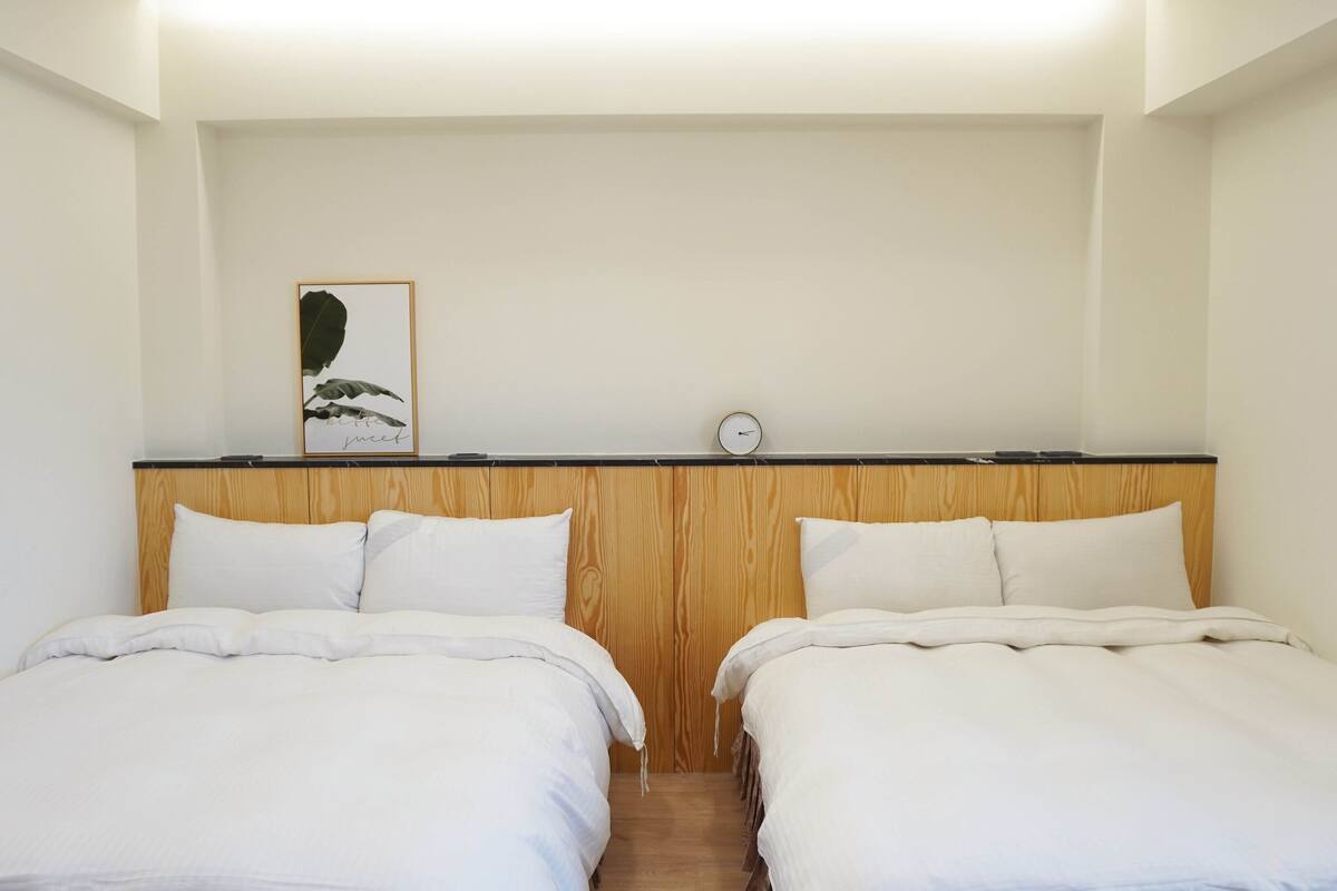 A room with two single beds, a wooden headboard, a framed picture, and a wall clock.