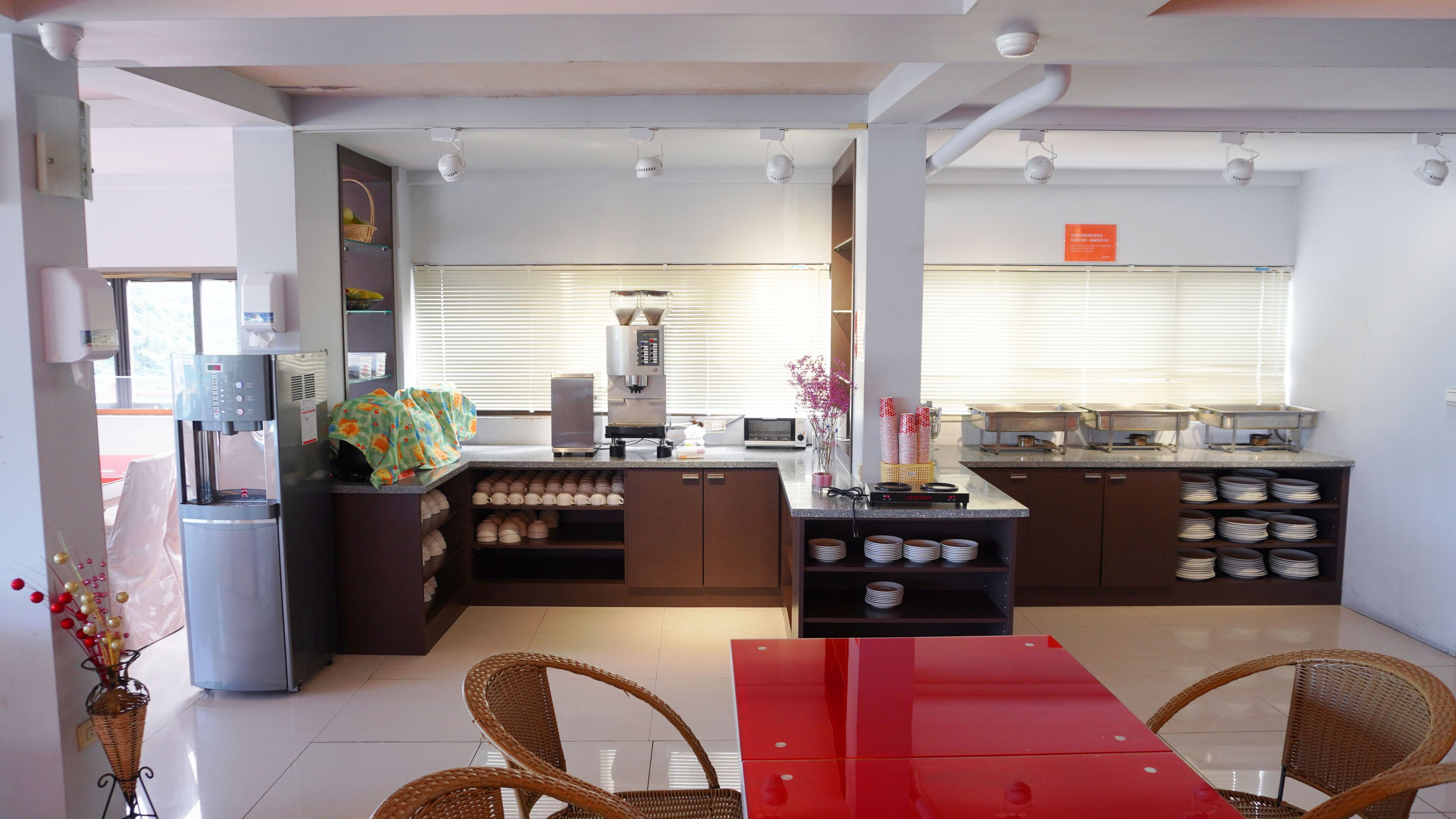 A modern kitchen with a red table, wicker chairs, and a coffee machine.