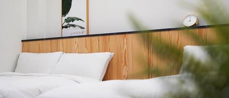 A bedroom with a wooden headboard, white bedding, a framed plant, and a clock.