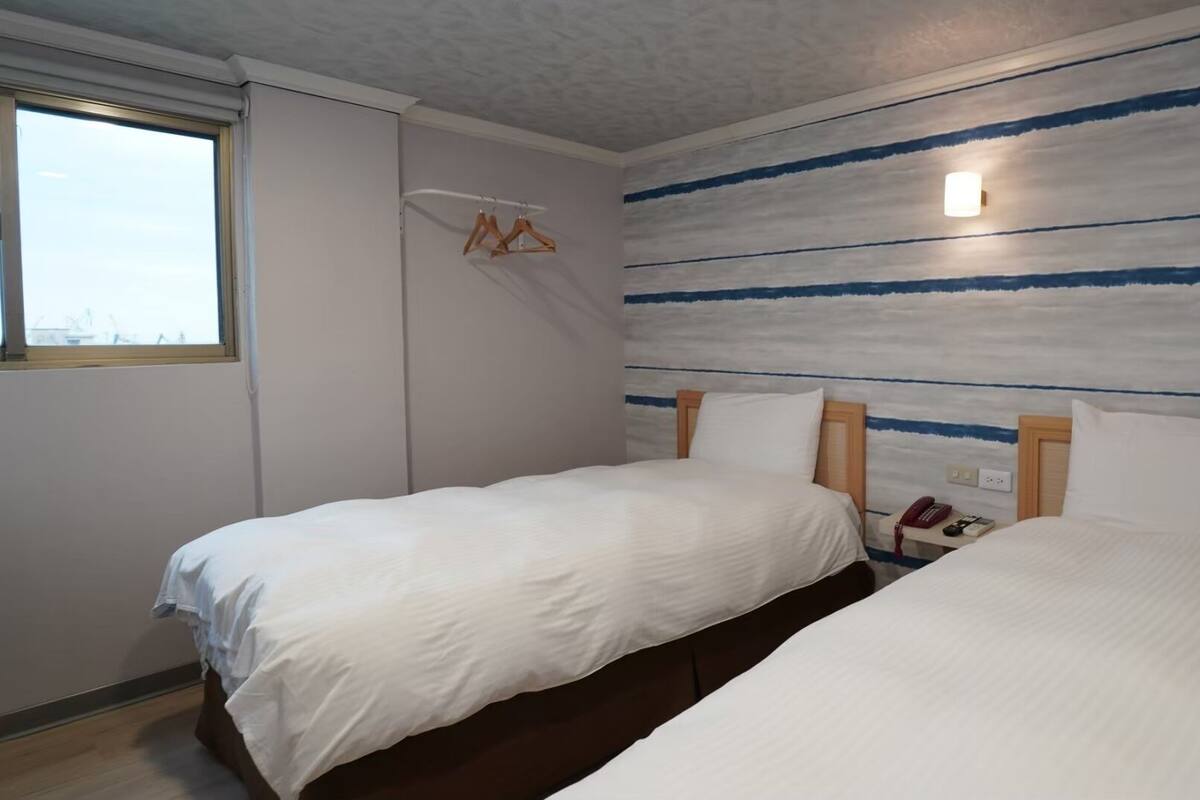 A room with two beds, a window, and a wall with horizontal stripes.