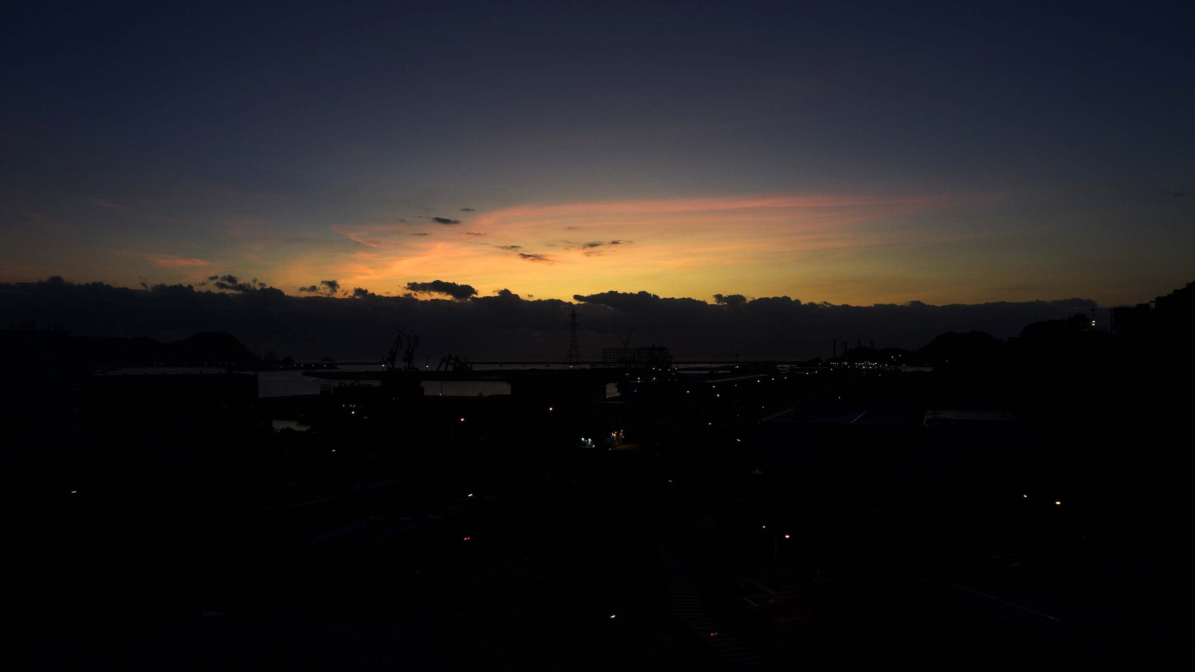 Solnedgang over et kystområde med industribygninger og en bro.