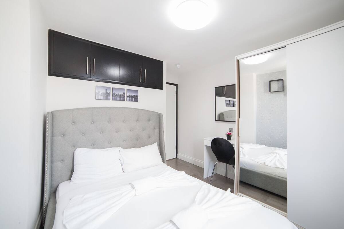 A bedroom with a bed, a desk, a chair, a wardrobe, and a mirror.
