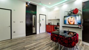 A modern kitchen with red cabinets, a dining area with a black and red table, and a TV mounted on the wall. - Imperial Court Suites (London)