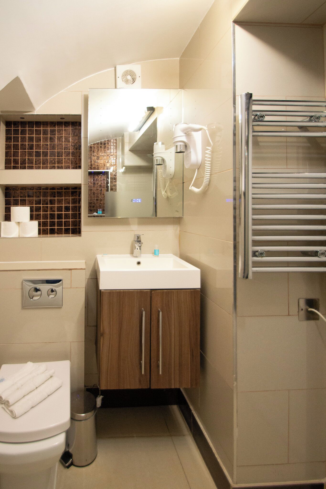 A modern bathroom with a white sink, wooden cabinets, a mirror, a towel rack, and a toilet.