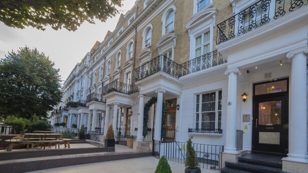 A row of traditional buildings with white facades, columns, and black iron balconies. - Imperial Court Suites (London)