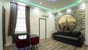 A modern living room with a stone wall mural, a black sofa, a dining table with red chairs, and a window with curtains. - Imperial Court Suites (London)